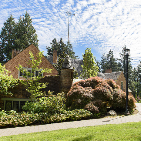 Exterior of Manor House with bushes, a green lawn, and a blue sky.
