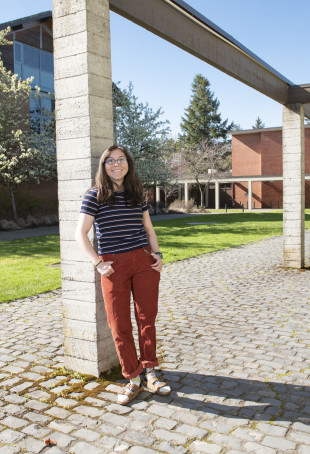 Cloe standing outside on the undergrad campus. She is wearing a blue striped top, red pants, and sandals with socks.