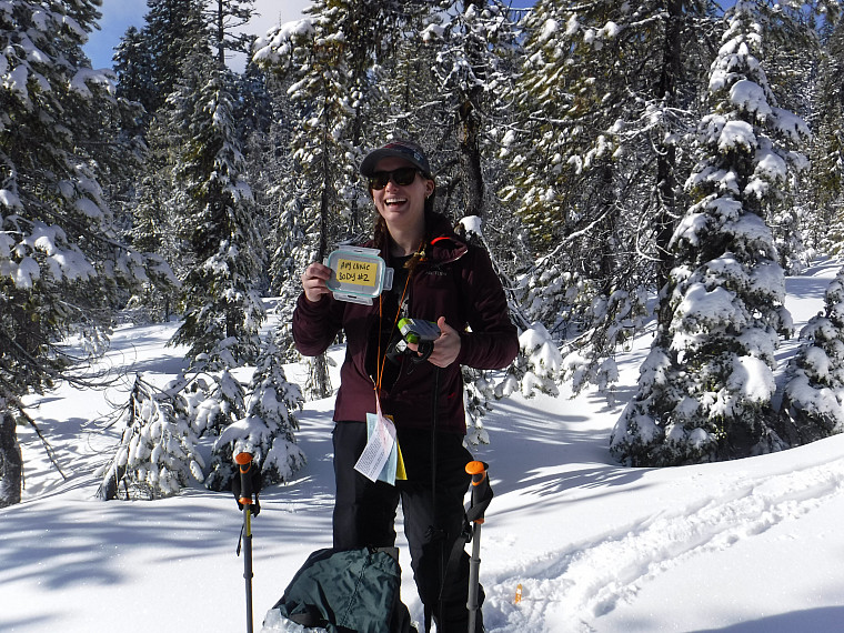 Participant poses with avalanche safety equipment with snow behind them.