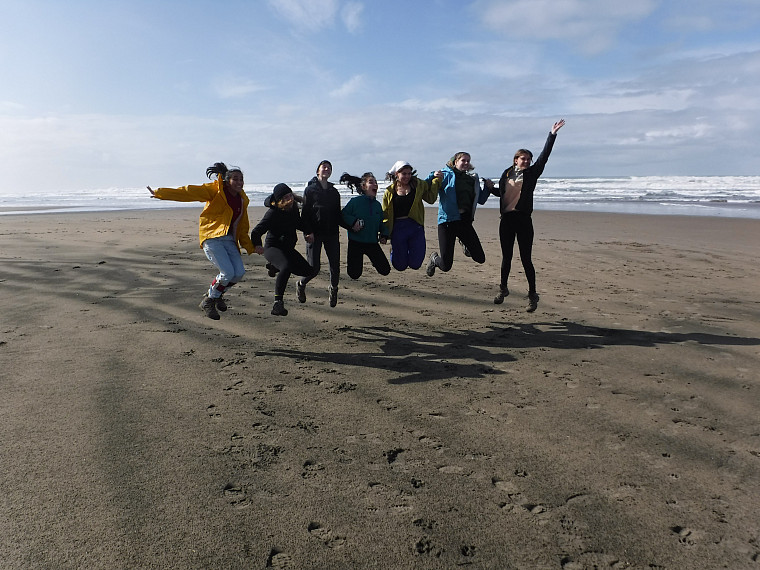 Participants jump in group on the coast with blue sky behind them.