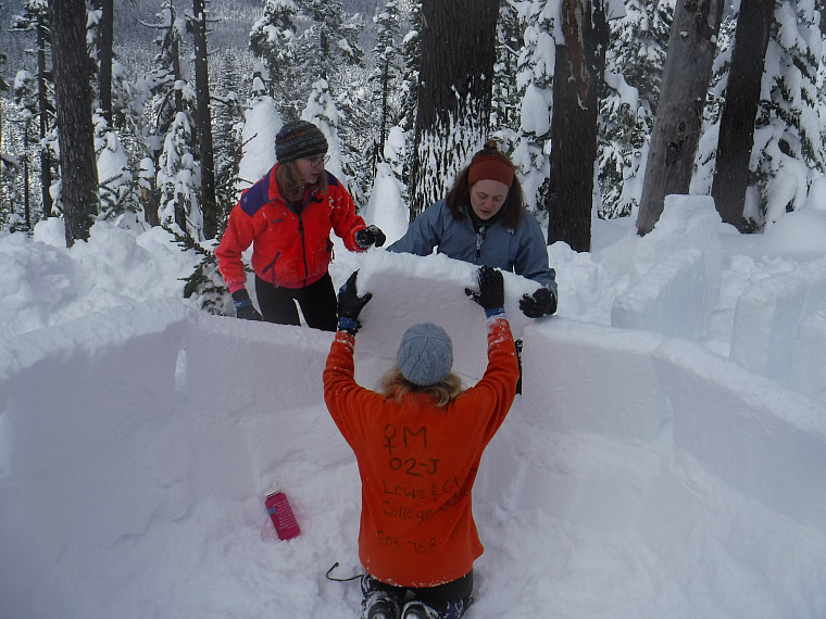 Participants in bright jackets work on building an igloo together.