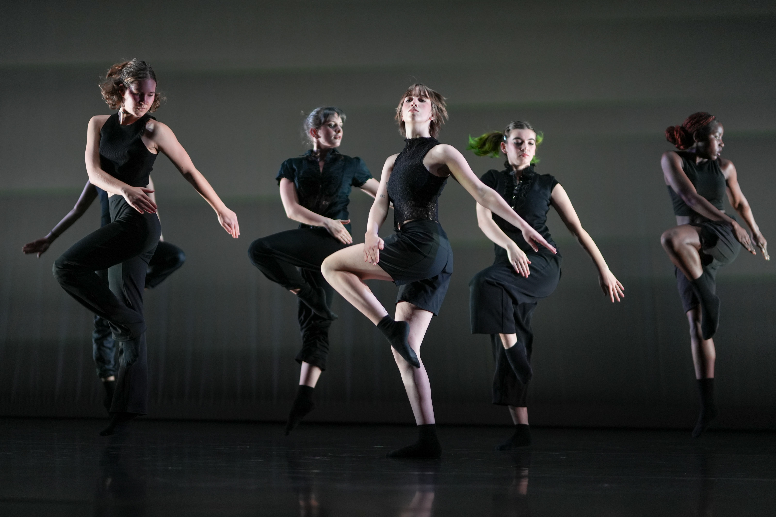 Students dancing against a grey background. They are wearing black clothes and black socks.