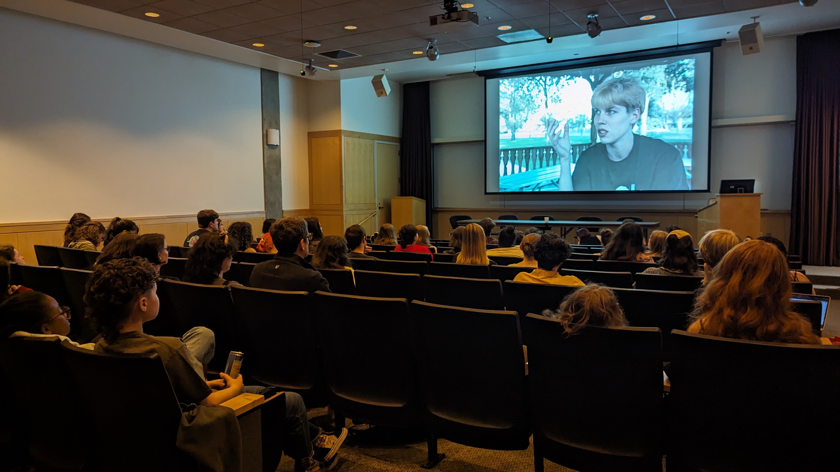 A large group of people sitting in a theater with a film on the big screen.