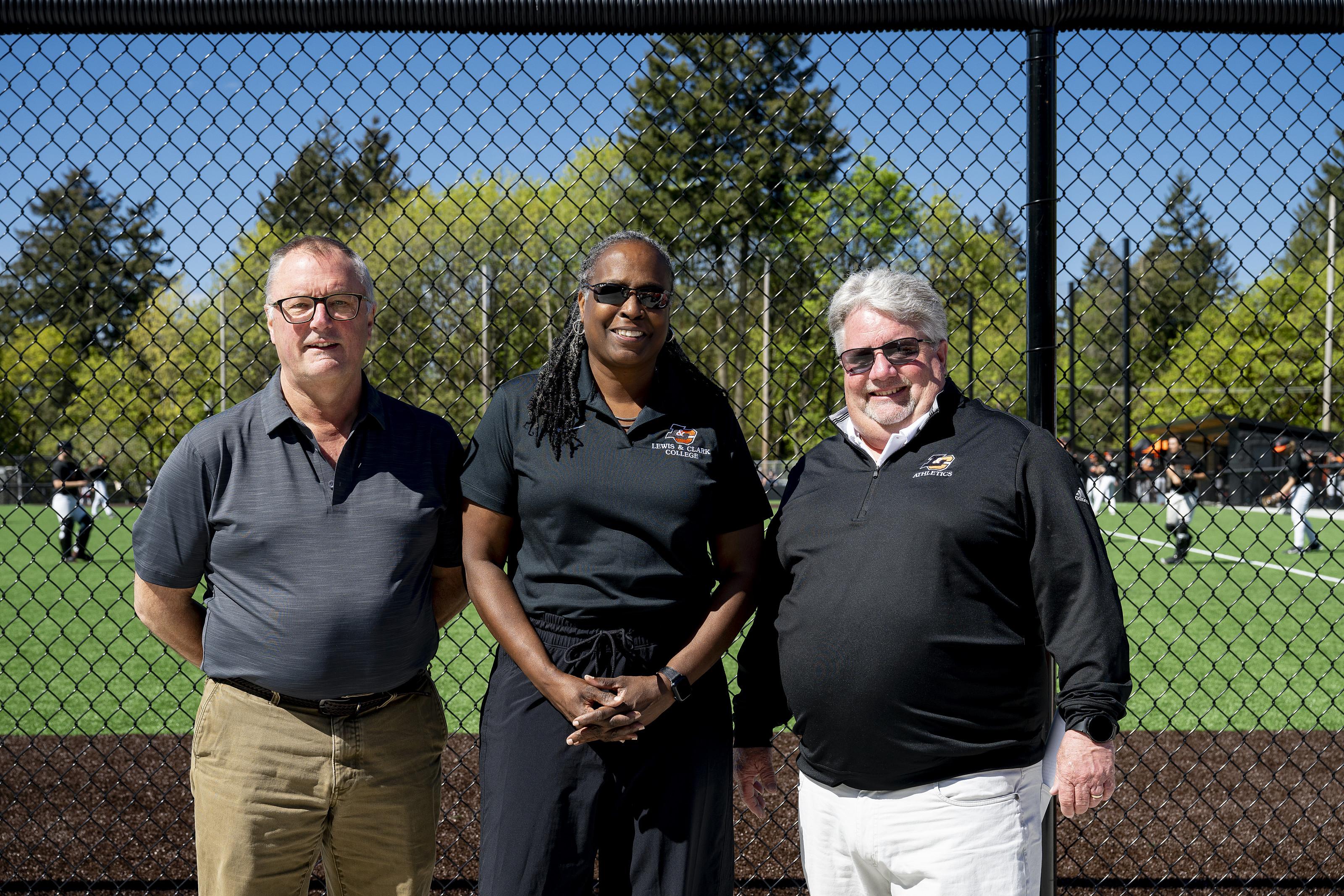 President Robin Holmes-Sullivan poses with Mark Pietrok and Jim Spencer BA '85 in front of the baseball diamond.