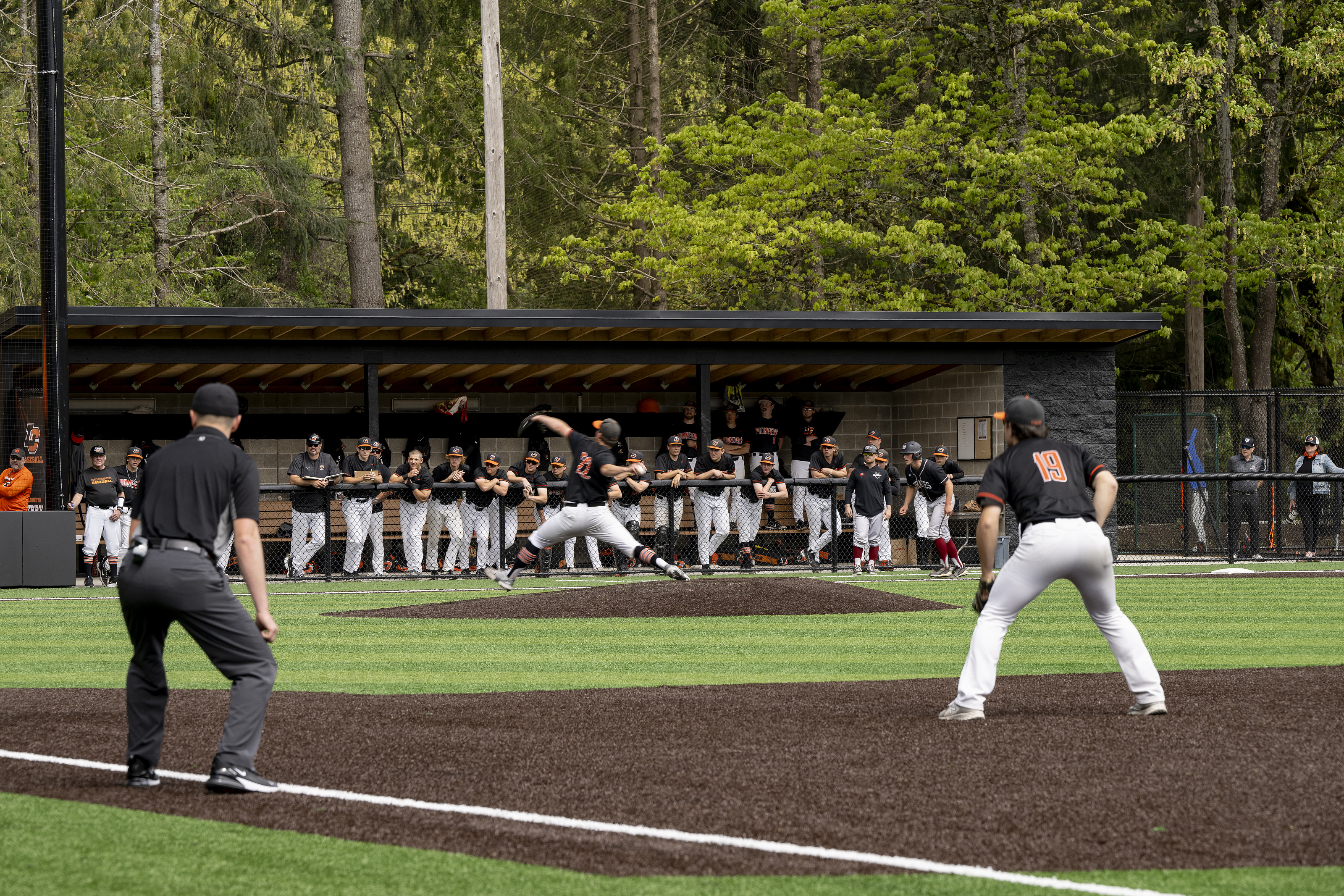 Baseball player throwing a ball during the game while his teammates watch from the dugout.