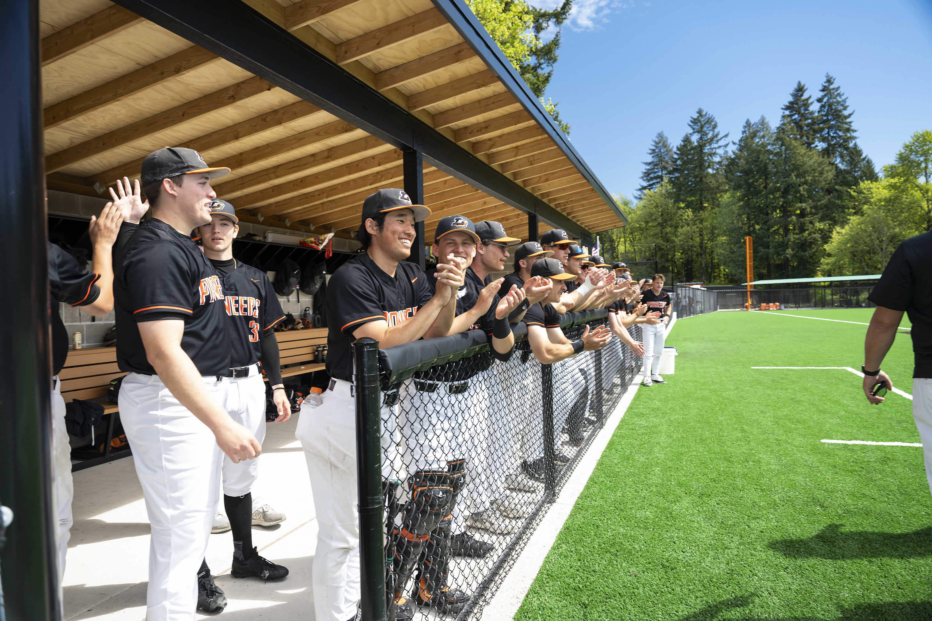 Baseball players standing at the edge of their dugout, watching the game and clapping.