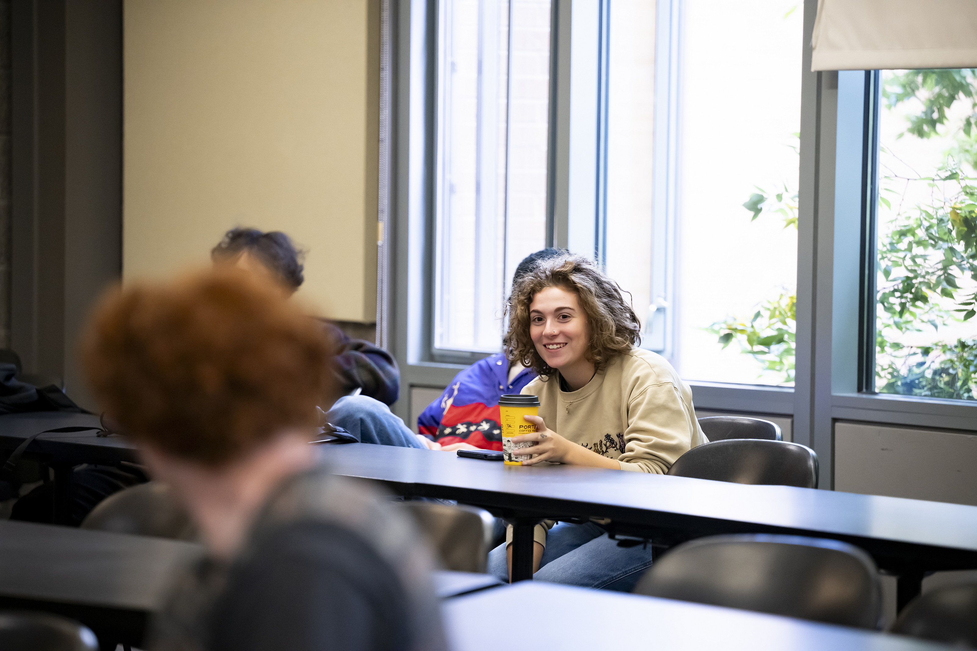 A student in a classroom, talking and smiling.