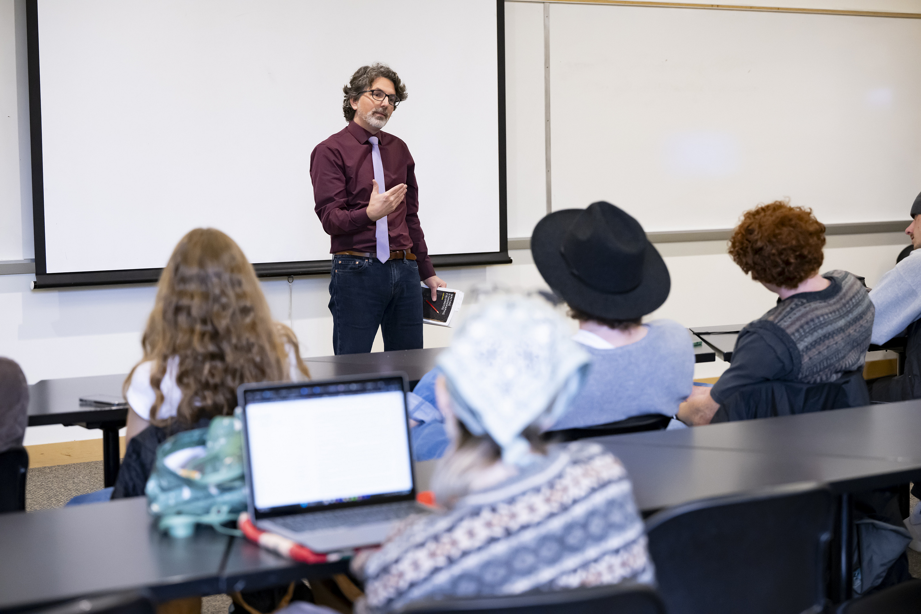 A professor stands talking in front of a room of students.