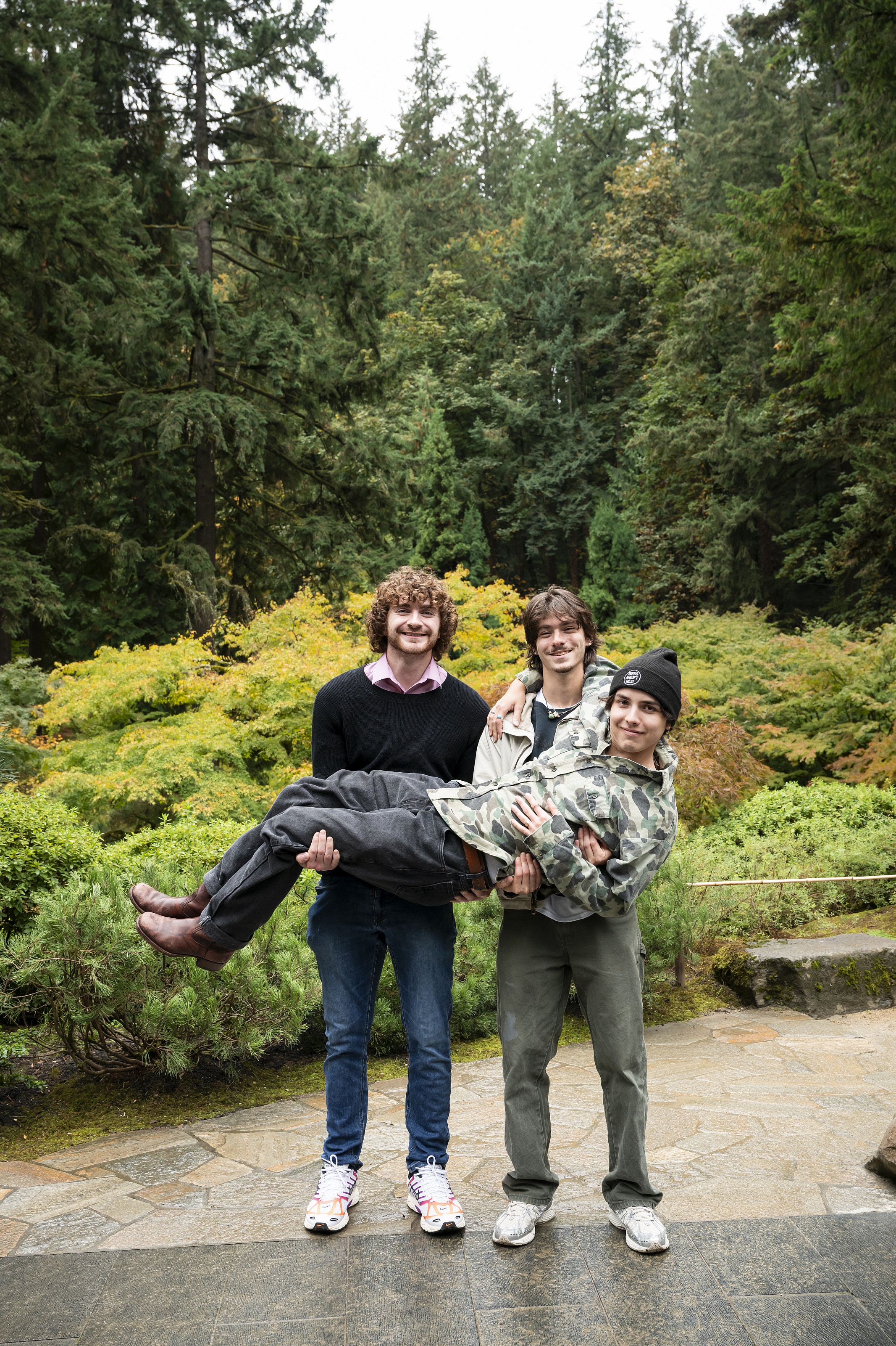 Two students hold up another student while surrounded by green trees.