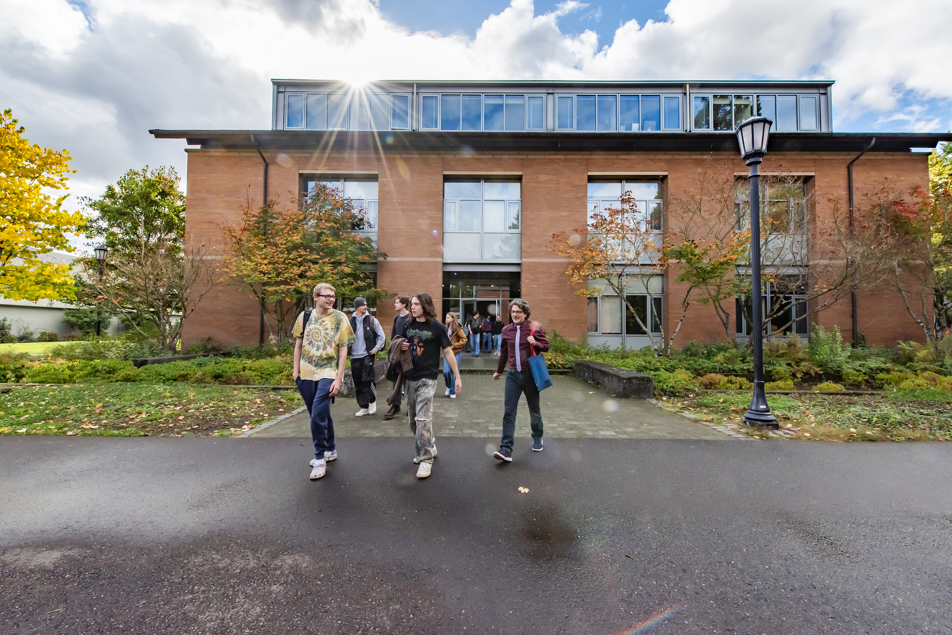 Students and a faculty member walking out of a building with the sun shining behind them.