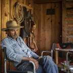 Max sitting on a chair, wearing a cowboy hat, denim button-up shirt, and jeans.