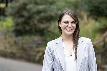 Andrea posing outside, wearing glasses and a white blazer.