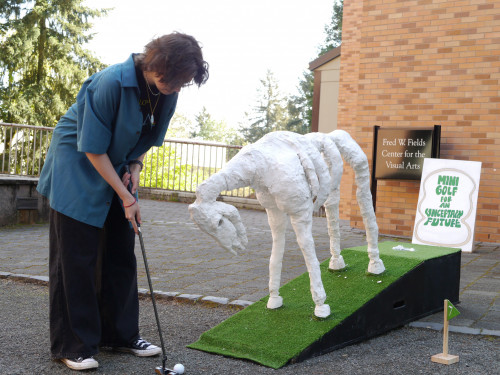 A student hits a golf ball up a ramp with a statue of a horse skeleton on it.