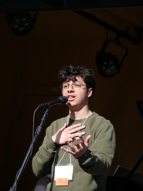 Nico singing on stage, wearing a long-sleeve green shirt and glasses.