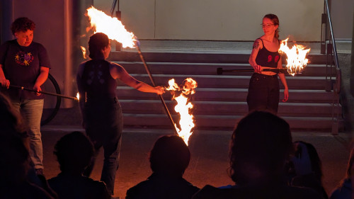 Three students holding large sticks with fire on the end.